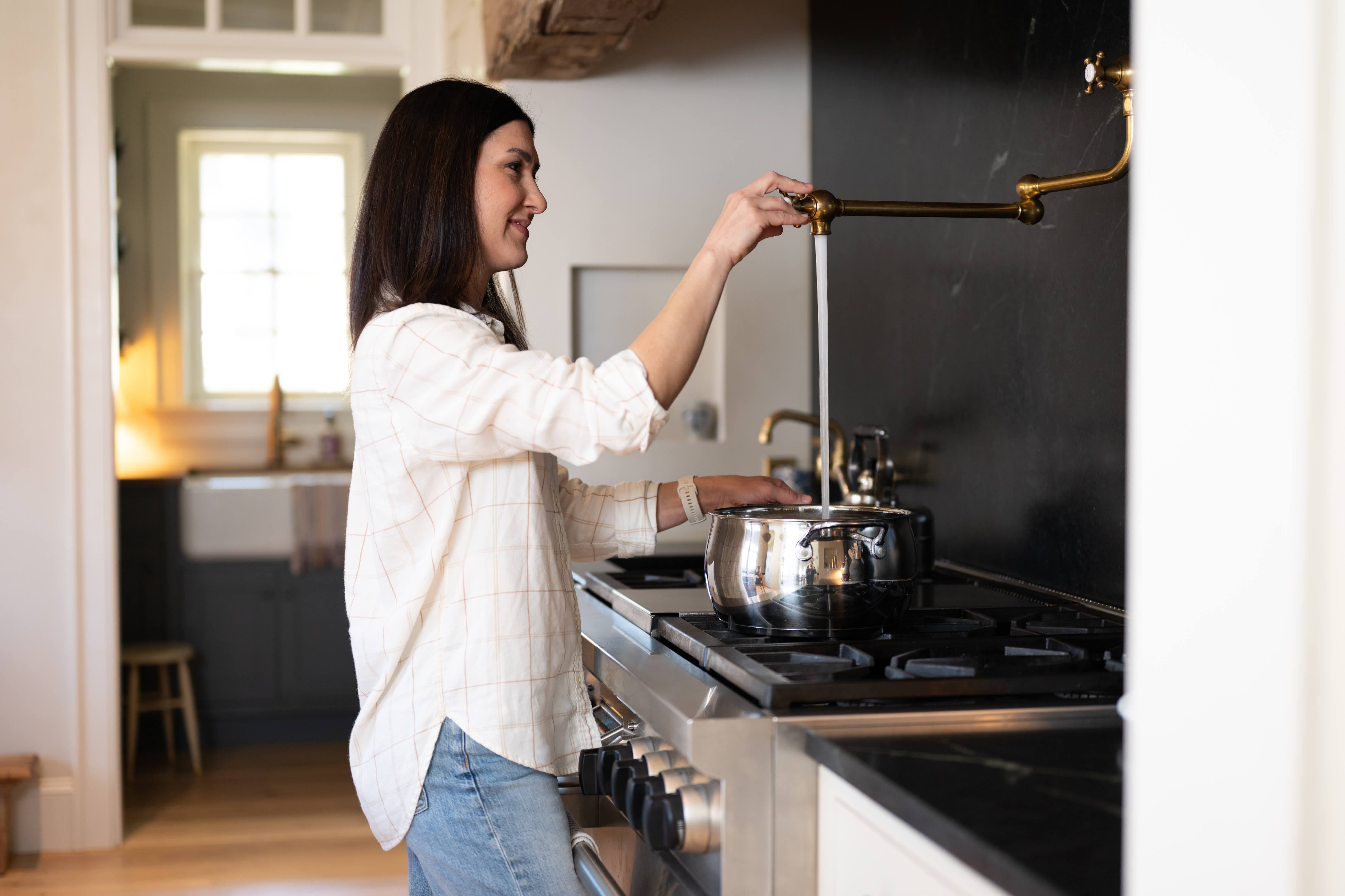 Woman in kitchen filling pot with water